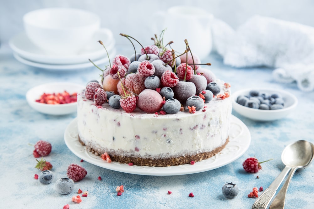 Cheesecake na bílém talíři ozdobený mraženými borůvkami, malinami a višněmi